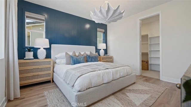 bedroom featuring a spacious closet, wood finished floors, and baseboards