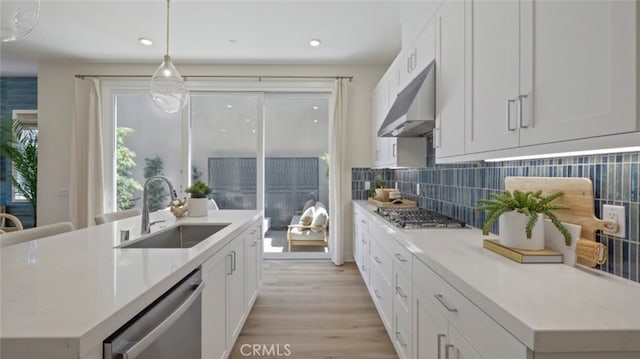 kitchen with white cabinets, appliances with stainless steel finishes, a sink, under cabinet range hood, and backsplash