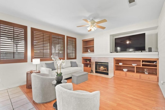 living area with built in shelves, a fireplace, visible vents, ceiling fan, and wood finished floors