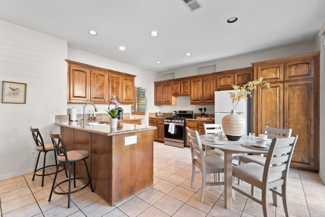 kitchen with a peninsula, a sink, visible vents, freestanding refrigerator, and stainless steel range with gas stovetop