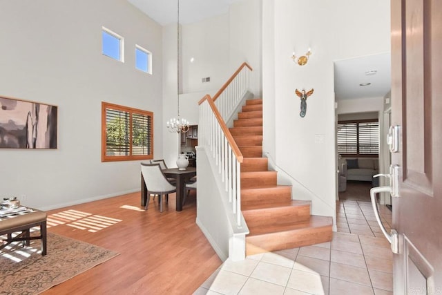 stairs featuring a notable chandelier, visible vents, a high ceiling, wood finished floors, and baseboards