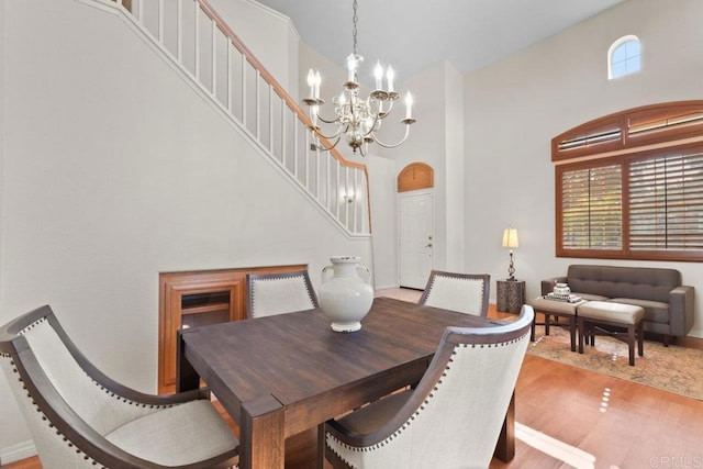 dining area with arched walkways, wood finished floors, a towering ceiling, and a chandelier