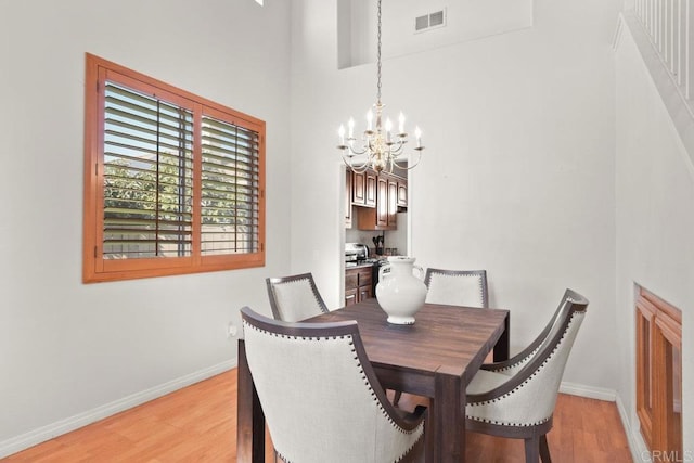 dining room with a notable chandelier, a high ceiling, visible vents, baseboards, and light wood-style floors