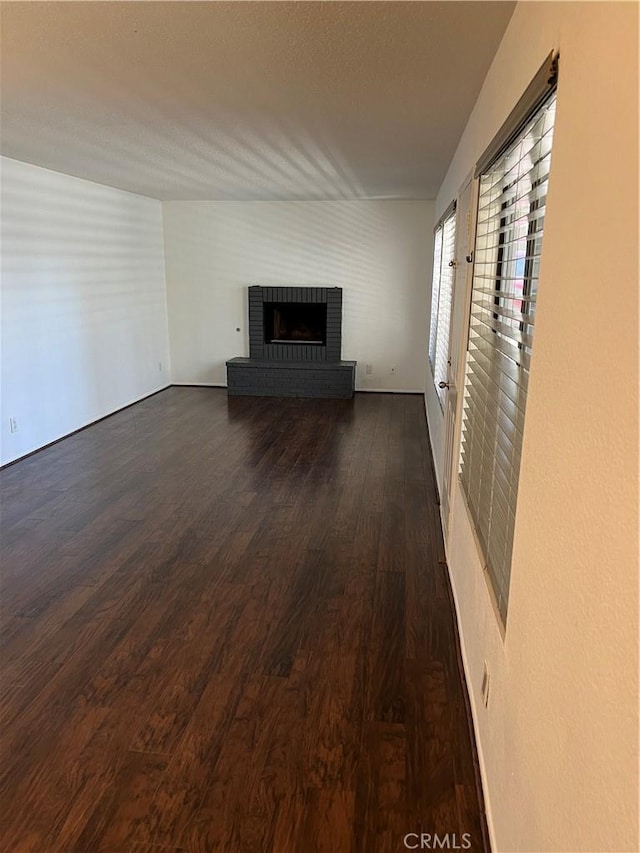 unfurnished living room with dark wood-style flooring and a brick fireplace