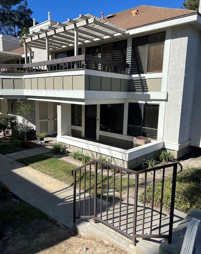 rear view of house with a balcony, roof with shingles, a pergola, and stucco siding