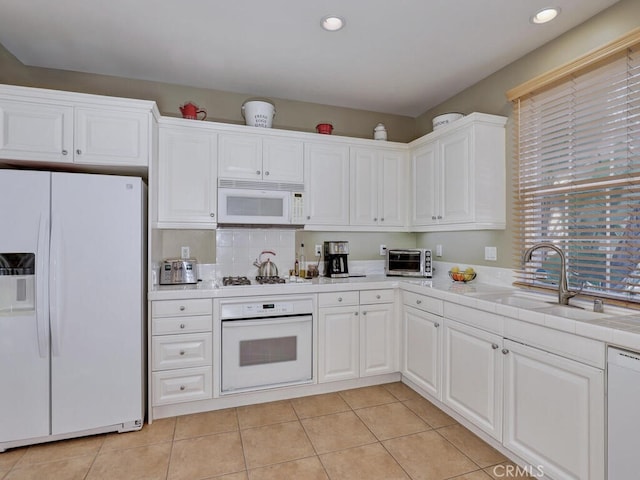 kitchen featuring white appliances, a toaster, white cabinets, light countertops, and a sink