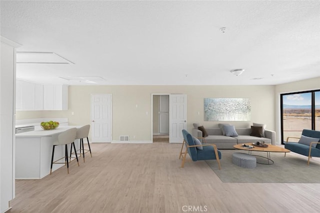 living room with baseboards, a textured ceiling, visible vents, and light wood-style floors