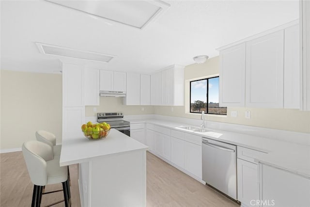 kitchen featuring under cabinet range hood, a sink, light countertops, appliances with stainless steel finishes, and a kitchen bar