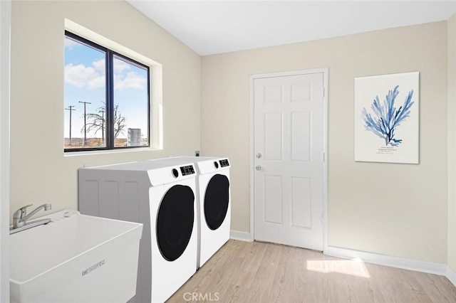 laundry room with light wood-style floors, a sink, washer and dryer, laundry area, and baseboards