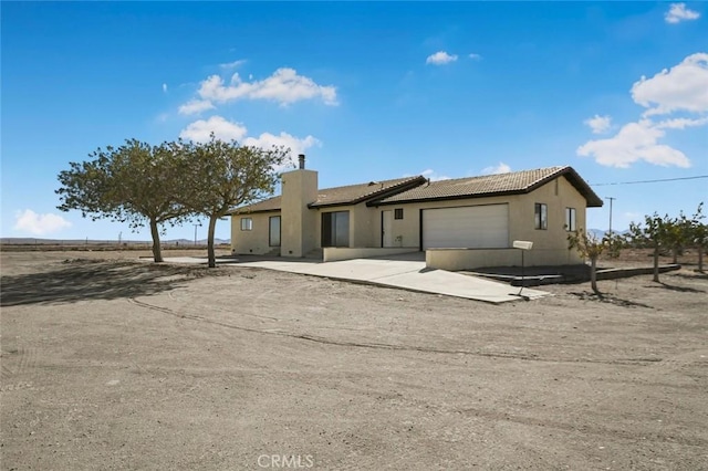 single story home with a chimney, stucco siding, an attached garage, driveway, and a tiled roof