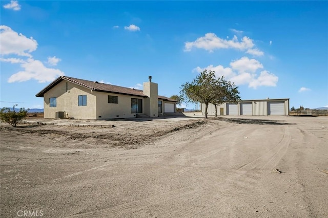 back of property featuring a garage, a chimney, an outbuilding, and stucco siding