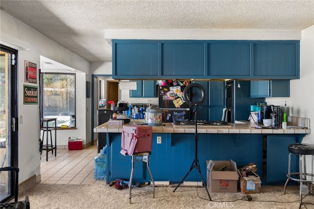 kitchen with tile countertops, blue cabinetry, and a breakfast bar area