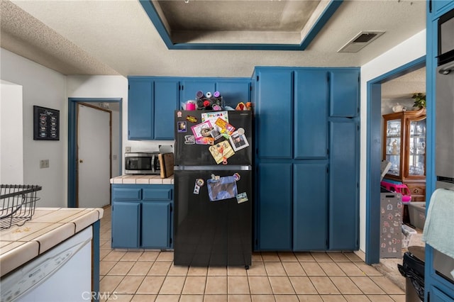 kitchen featuring tile counters, stainless steel microwave, visible vents, freestanding refrigerator, and blue cabinets