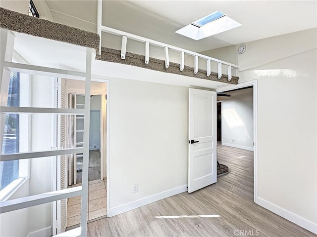 unfurnished room featuring lofted ceiling with skylight, light wood-style flooring, and baseboards