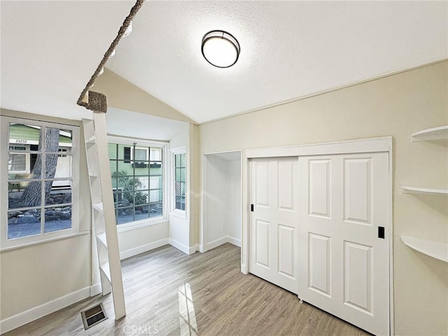 unfurnished bedroom with baseboards, visible vents, lofted ceiling, wood finished floors, and a closet