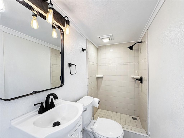 full bath with a textured wall, toilet, a tile shower, a textured ceiling, and a sink