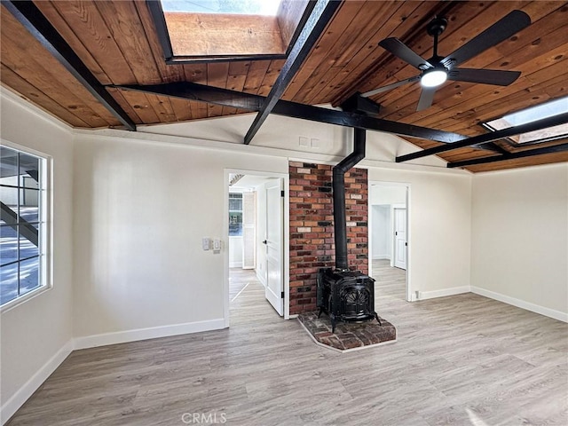 unfurnished living room featuring lofted ceiling with skylight, a wood stove, baseboards, and wood finished floors