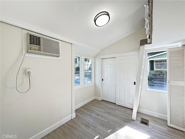 foyer with baseboards, visible vents, wood finished floors, vaulted ceiling, and an AC wall unit