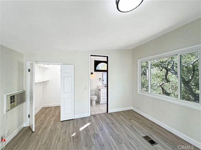 unfurnished bedroom with a wall unit AC, visible vents, a spacious closet, wood finished floors, and baseboards