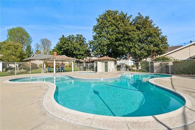 pool with an outbuilding, a patio area, fence, and a hot tub