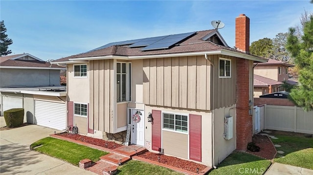 view of front facade featuring concrete driveway, a chimney, fence, roof mounted solar panels, and board and batten siding