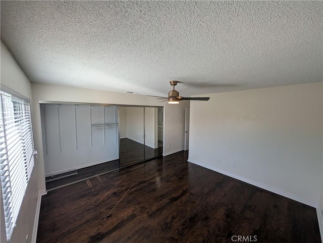 unfurnished bedroom featuring a textured ceiling, a closet, visible vents, and dark wood-style flooring