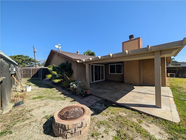 back of house featuring a chimney, stucco siding, an outdoor fire pit, a patio area, and a fenced backyard