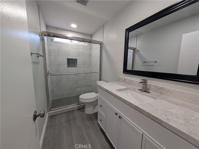 bathroom featuring toilet, wood finished floors, visible vents, vanity, and a shower stall