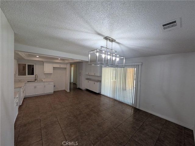 unfurnished dining area with a textured ceiling, a raised ceiling, a sink, and visible vents