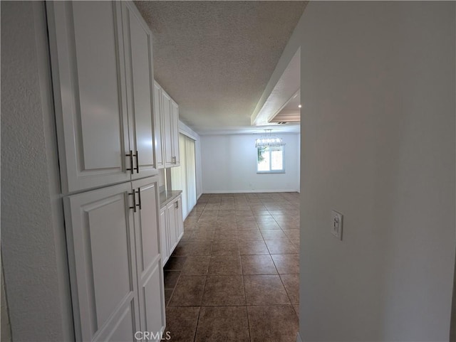 hall featuring a textured ceiling, dark tile patterned floors, and baseboards