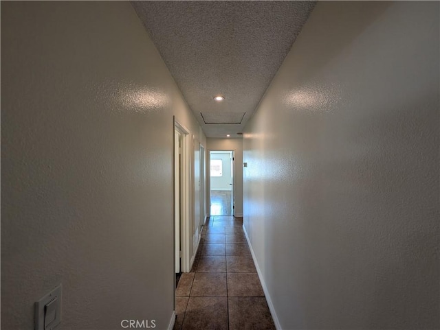 corridor featuring a textured wall, baseboards, a textured ceiling, and tile patterned floors