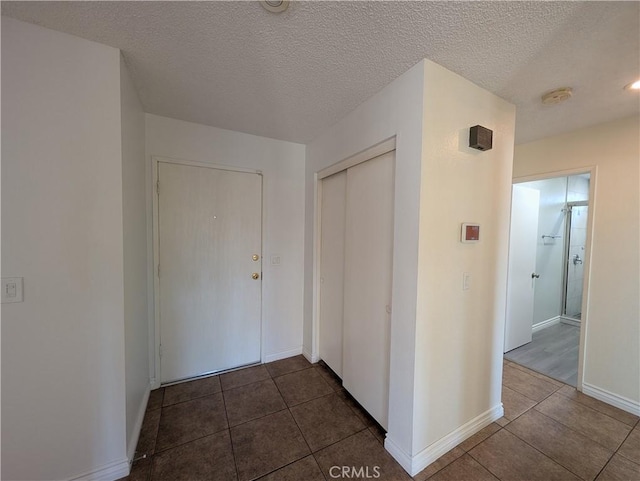 hallway with dark tile patterned floors, baseboards, and a textured ceiling