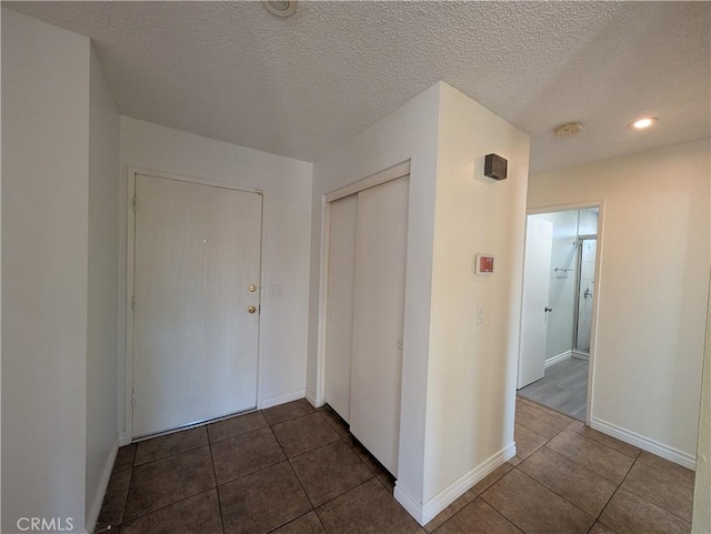 corridor featuring a textured ceiling, dark tile patterned floors, and baseboards