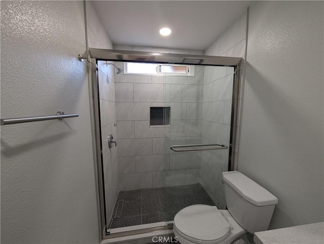 bathroom featuring toilet, a shower stall, and a textured wall