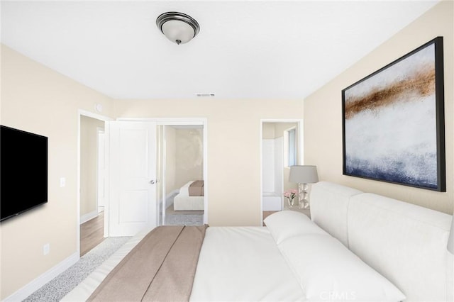 bedroom featuring ensuite bath, visible vents, and baseboards