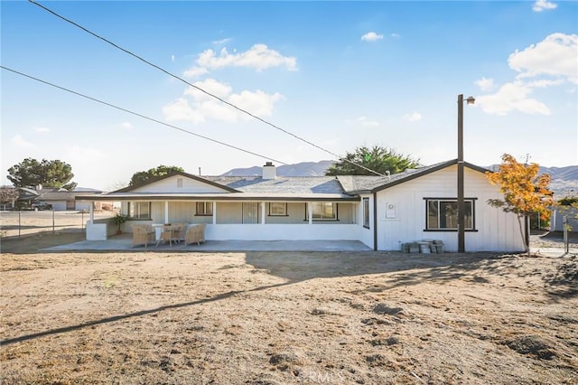 back of property featuring a chimney, fence, a mountain view, and a patio