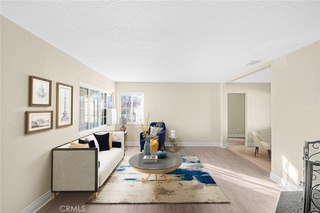 living room with a textured ceiling, wood finished floors, visible vents, and baseboards