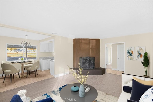 living room featuring light wood-style flooring, a fireplace, visible vents, and an inviting chandelier