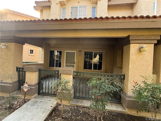 doorway to property with a porch, fence, a gate, and stucco siding