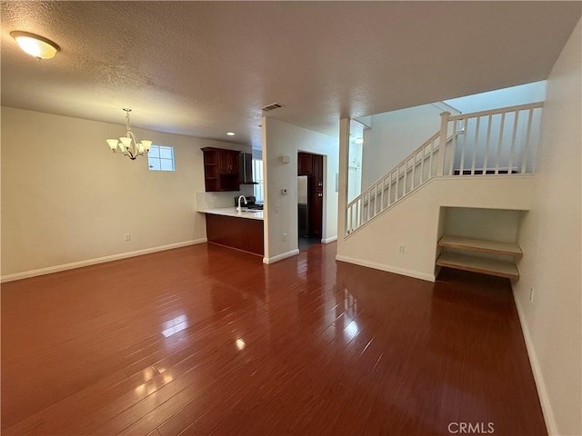 unfurnished living room featuring baseboards, visible vents, dark wood finished floors, stairs, and a chandelier