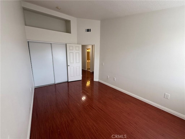 unfurnished bedroom featuring baseboards, visible vents, dark wood finished floors, and a closet