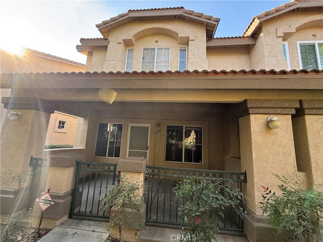 entrance to property featuring covered porch, a gate, fence, and stucco siding