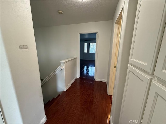 hallway featuring baseboards, dark wood finished floors, a textured ceiling, and an upstairs landing