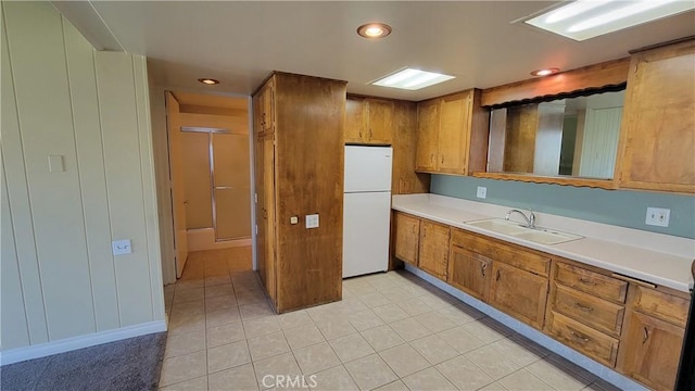 kitchen featuring brown cabinets, recessed lighting, light countertops, freestanding refrigerator, and a sink