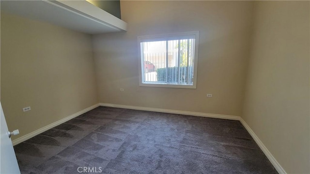 spare room with baseboards and dark carpet