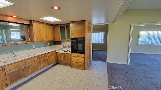 kitchen with brown cabinetry, light colored carpet, black oven, and a sink