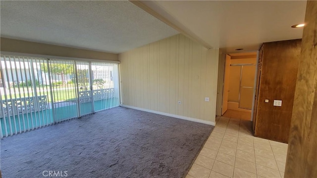 unfurnished room with light tile patterned floors, a textured ceiling, baseboards, and light colored carpet