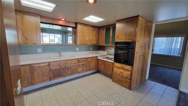 kitchen with light countertops, brown cabinetry, a sink, and oven