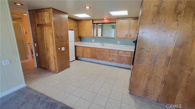 kitchen featuring light tile patterned floors, a sink, light countertops, freestanding refrigerator, and brown cabinets