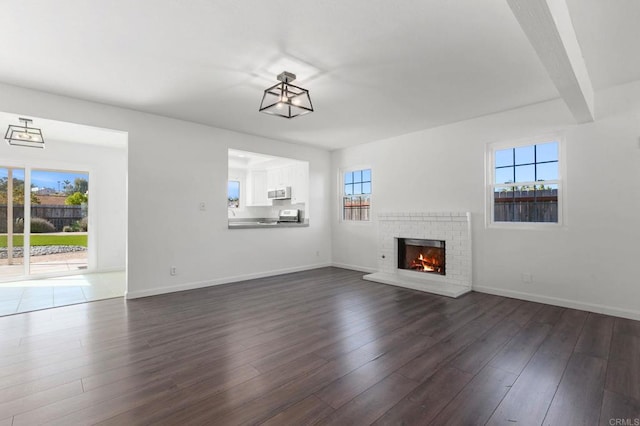 unfurnished living room featuring a brick fireplace, baseboards, dark wood-style flooring, and beamed ceiling